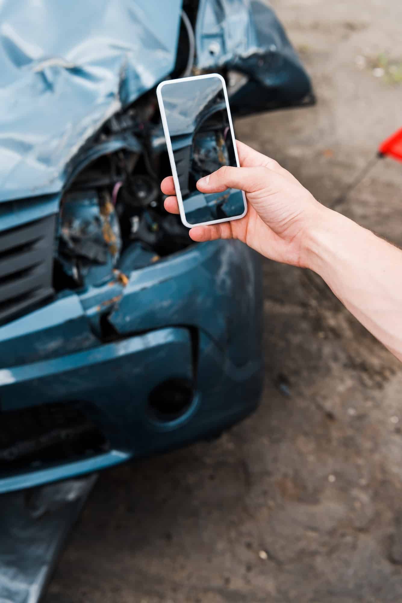 cropped view of man holding smartphone with blank screen near damaged car